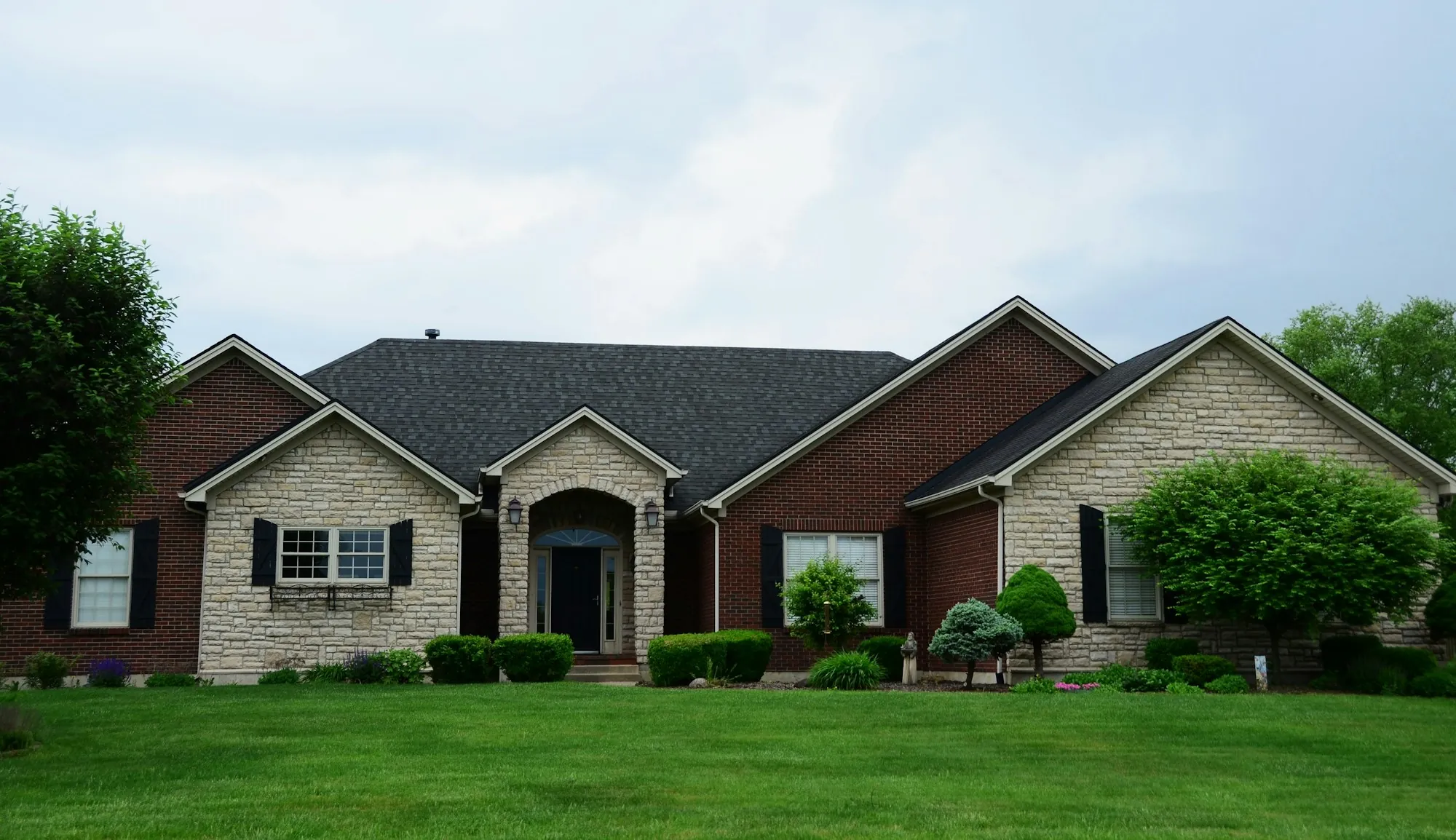 Brick and stone ranch home with green shrubs